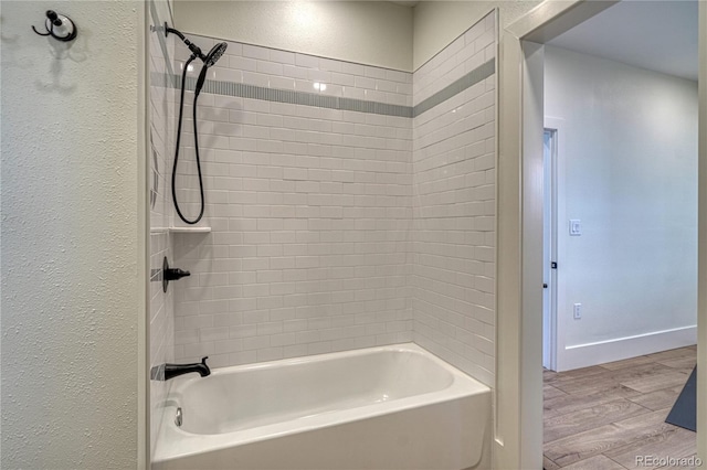 bathroom with shower / bathing tub combination, baseboards, wood finished floors, and a textured wall