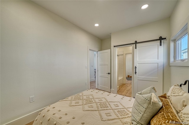 bedroom with recessed lighting, baseboards, a barn door, and wood finished floors