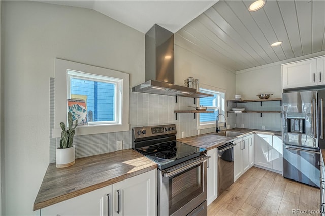 kitchen featuring open shelves, butcher block counters, appliances with stainless steel finishes, wall chimney exhaust hood, and a sink