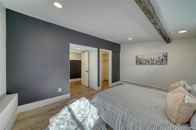 bedroom with a walk in closet, beamed ceiling, wood finished floors, recessed lighting, and baseboards