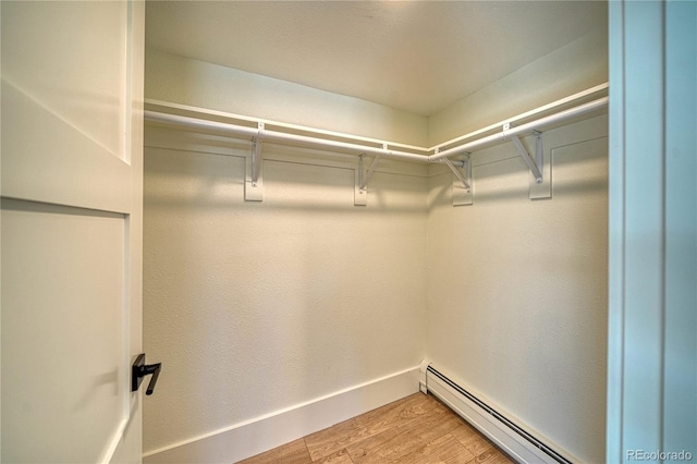 spacious closet with light wood finished floors and a baseboard radiator