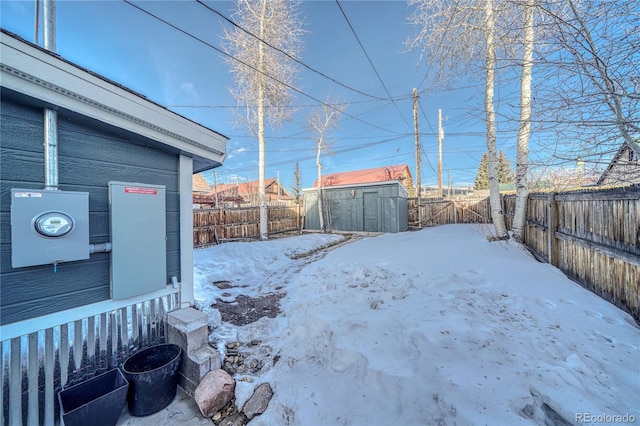 yard layered in snow with a storage unit, a fenced backyard, and an outdoor structure