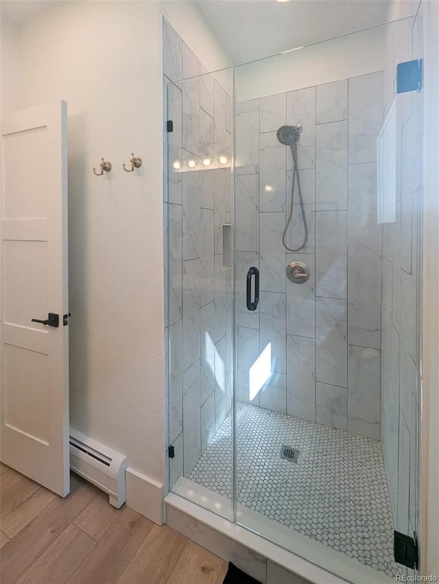 bathroom with a stall shower, a baseboard heating unit, baseboards, and wood finished floors