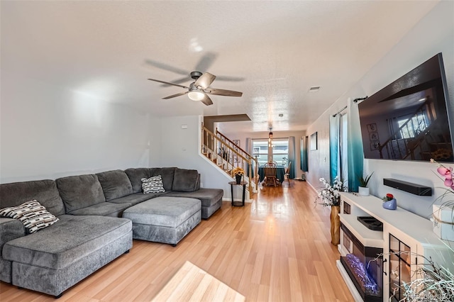 living room featuring ceiling fan, stairway, visible vents, and light wood-style floors