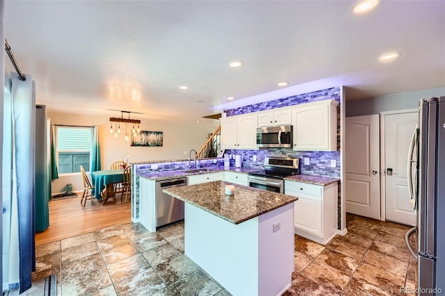 kitchen featuring a peninsula, white cabinetry, hanging light fixtures, appliances with stainless steel finishes, and a center island