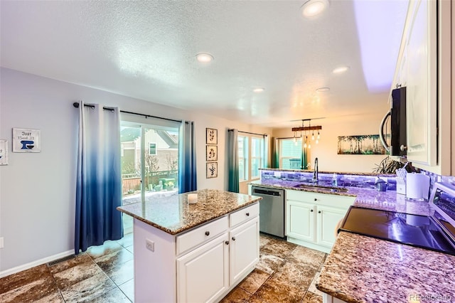 kitchen featuring appliances with stainless steel finishes, a center island, light stone countertops, white cabinetry, and a sink