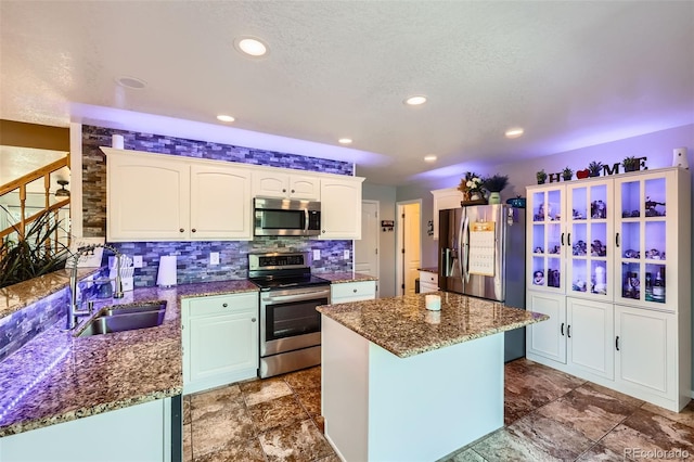 kitchen with stainless steel appliances, white cabinets, a sink, a kitchen island, and dark stone countertops