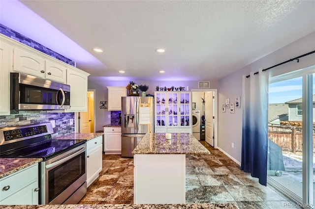 kitchen with appliances with stainless steel finishes, a center island, washer / clothes dryer, and white cabinets