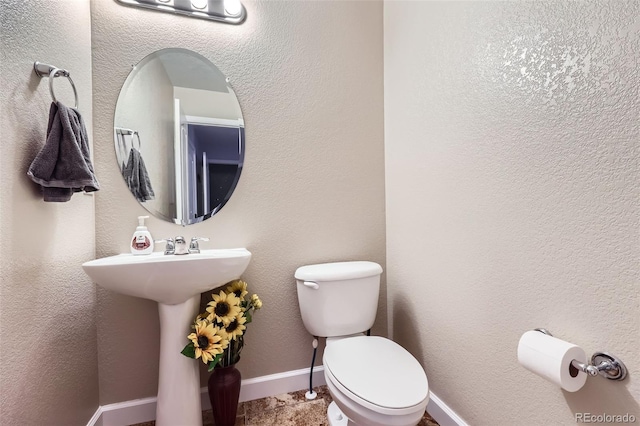 bathroom with baseboards, a textured wall, and toilet