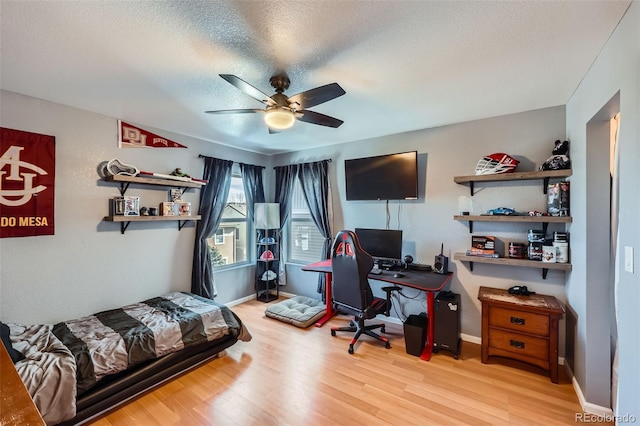 bedroom featuring a textured ceiling, ceiling fan, light wood-type flooring, and baseboards