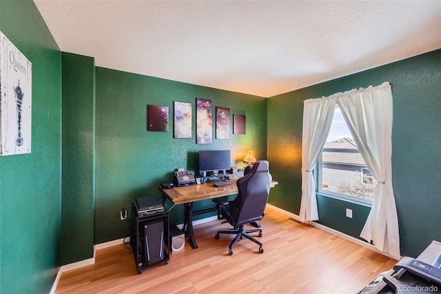 office space featuring a textured wall, light wood finished floors, and baseboards