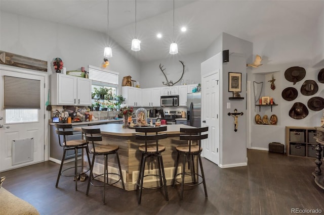 kitchen with appliances with stainless steel finishes, dark wood-style floors, white cabinets, and a kitchen breakfast bar