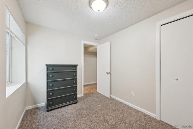 unfurnished bedroom with a closet, a textured ceiling, baseboards, and carpet floors