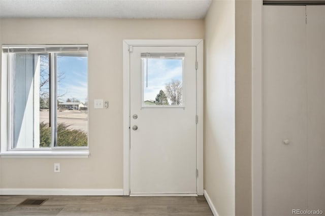 doorway with wood finished floors, a healthy amount of sunlight, visible vents, and baseboards