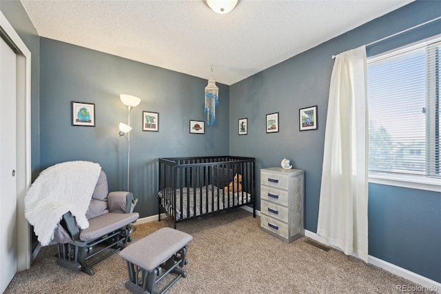 carpeted bedroom featuring a crib, visible vents, baseboards, and a textured ceiling