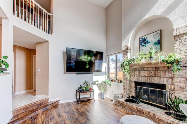living area featuring a towering ceiling, wood finished floors, a brick fireplace, and baseboards