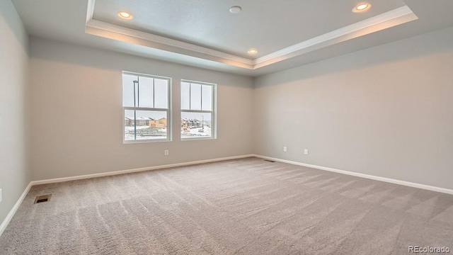 empty room featuring carpet floors, a tray ceiling, visible vents, and baseboards