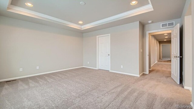 unfurnished bedroom featuring ornamental molding, a tray ceiling, visible vents, and carpet