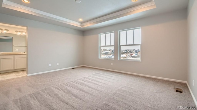 unfurnished bedroom featuring baseboards, visible vents, a raised ceiling, and light colored carpet