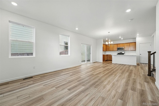 2116 Chambers Rd, Brighton, CO 80601 - unfurnished living room with visible vents, recessed lighting, an inviting chandelier, light wood-style flooring, and baseboards