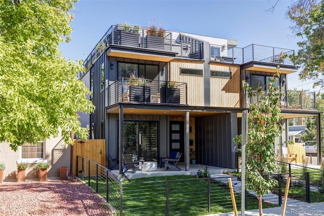 back of house with a balcony, a patio area, and a lawn