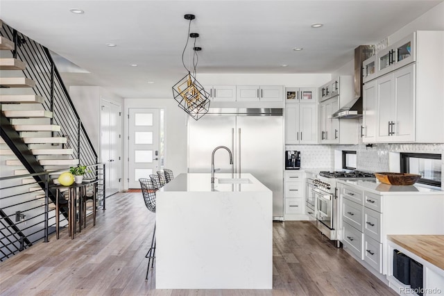 kitchen with wall chimney exhaust hood, decorative light fixtures, white cabinetry, and premium appliances