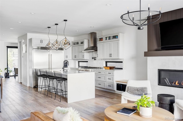 kitchen with range, wall chimney exhaust hood, a kitchen bar, white cabinetry, and a kitchen island with sink