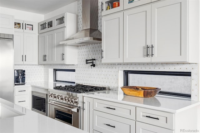 kitchen featuring white cabinetry, wall chimney exhaust hood, built in appliances, and tasteful backsplash