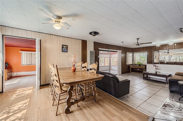 dining area with light wood-type flooring, ceiling fan, and wooden walls