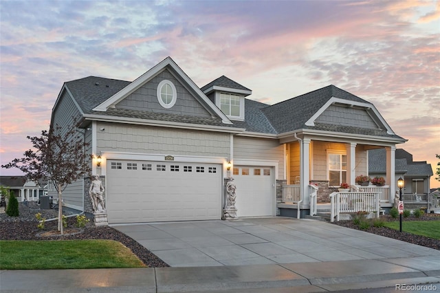 craftsman-style house with a shingled roof, a porch, concrete driveway, stone siding, and an attached garage