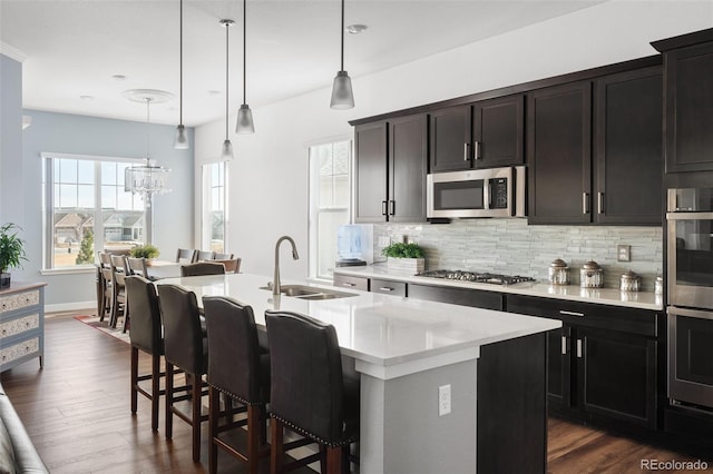 kitchen featuring a center island with sink, a sink, light countertops, appliances with stainless steel finishes, and tasteful backsplash