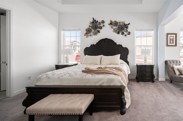 carpeted bedroom featuring a tray ceiling and baseboards