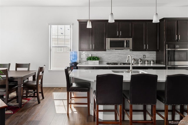 kitchen featuring dark wood-type flooring, appliances with stainless steel finishes, light countertops, decorative backsplash, and hanging light fixtures