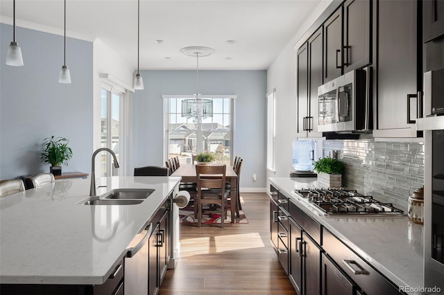 kitchen with light wood-style flooring, a sink, tasteful backsplash, appliances with stainless steel finishes, and an inviting chandelier