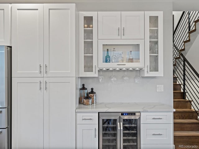 bar with stainless steel fridge, light stone counters, white cabinetry, and beverage cooler