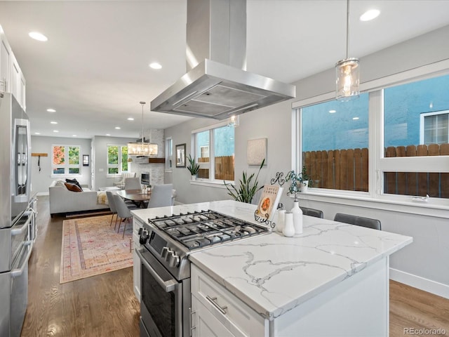 kitchen featuring island exhaust hood, white cabinetry, pendant lighting, and appliances with stainless steel finishes