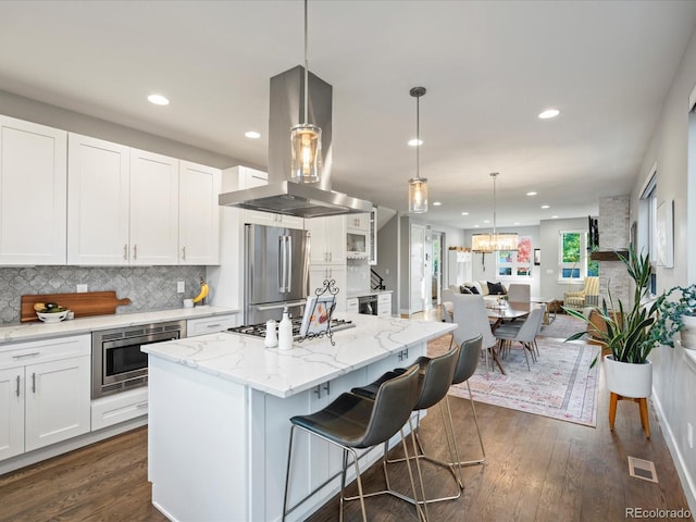 kitchen with a center island, stainless steel appliances, island exhaust hood, a kitchen bar, and white cabinets