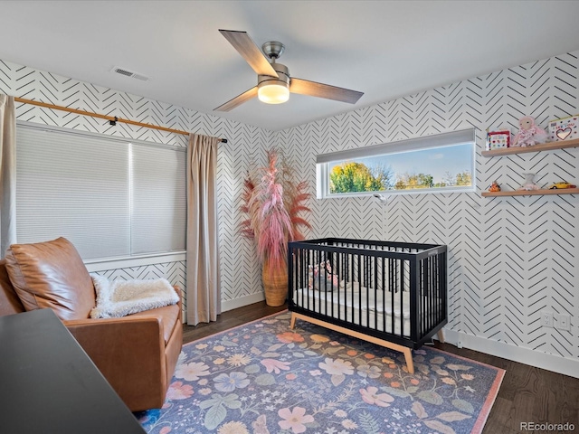 bedroom featuring ceiling fan, dark wood-type flooring, and a nursery area