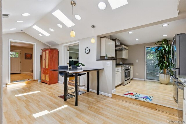 901 S Leyden St, Denver, CO 80224 - kitchen with stainless steel appliances, a skylight, wall chimney exhaust hood, white cabinets, and vaulted ceiling