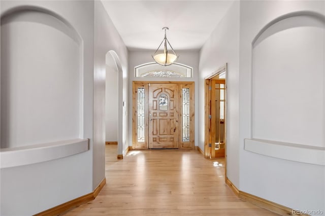 foyer with light wood-style floors, baseboards, and arched walkways