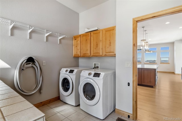 laundry area featuring cabinet space, light tile patterned floors, baseboards, washing machine and dryer, and a chandelier