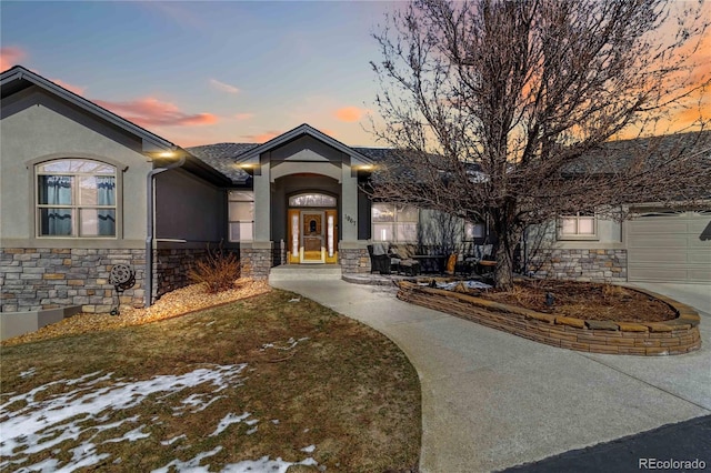 view of front of home featuring a garage, stone siding, and stucco siding