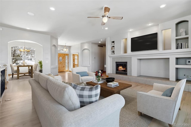 living area featuring arched walkways, a tile fireplace, light wood-style flooring, and recessed lighting