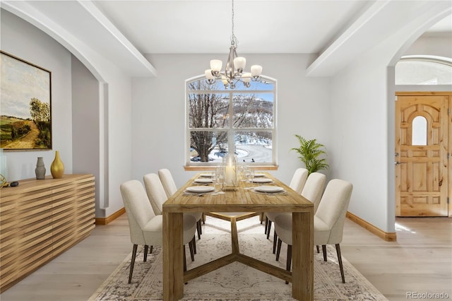 dining area featuring light wood finished floors, baseboards, a chandelier, and arched walkways