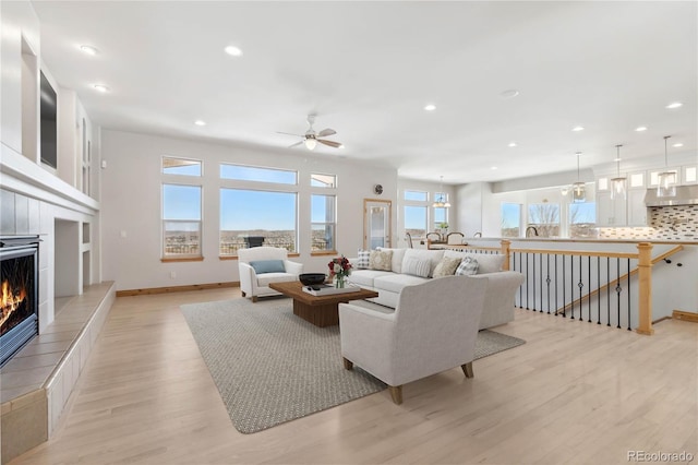 living room with a wealth of natural light, light wood-style flooring, a tiled fireplace, and recessed lighting