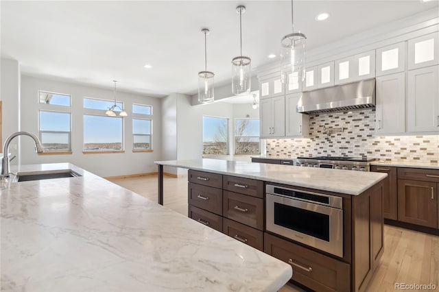 kitchen with a center island, a sink, under cabinet range hood, white cabinetry, and backsplash