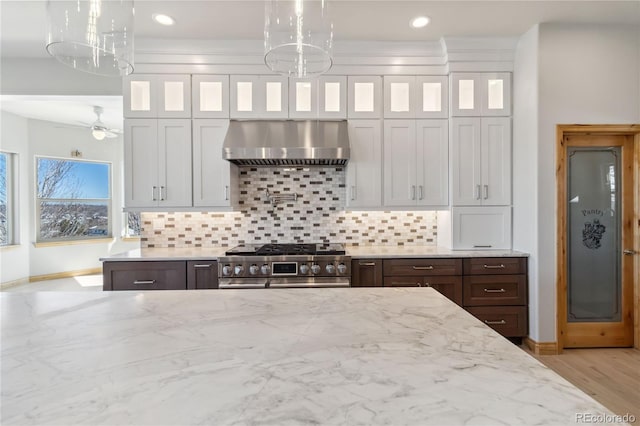 kitchen featuring high end stove, glass insert cabinets, extractor fan, and decorative backsplash