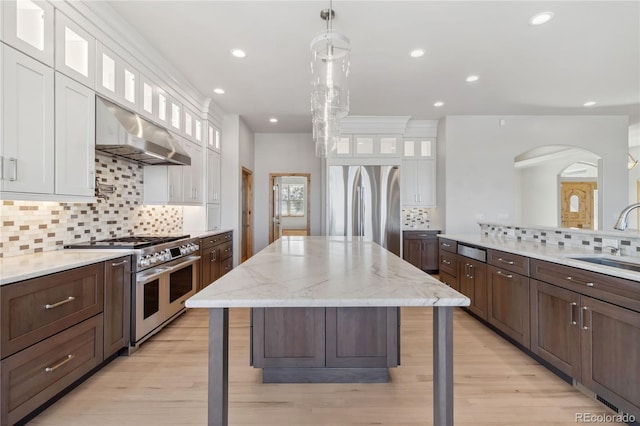 kitchen featuring stainless steel appliances, white cabinetry, a sink, a kitchen island, and under cabinet range hood