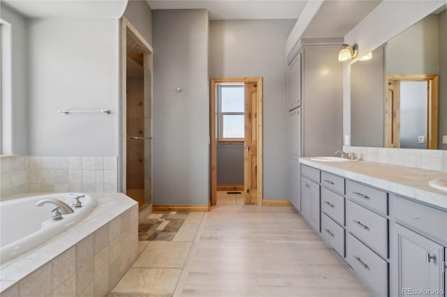 full bath featuring a garden tub, a sink, baseboards, tiled shower, and double vanity