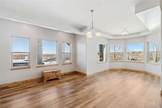 interior space featuring a raised ceiling, baseboards, an inviting chandelier, and wood finished floors